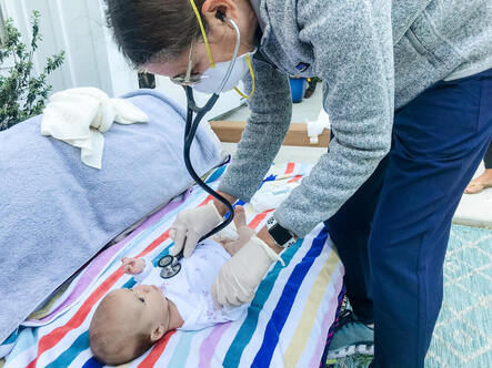 Doctor examining baby on outdoor couch and stripped blanket