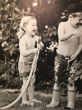 Black and white photo of girl spraying boy with a hose